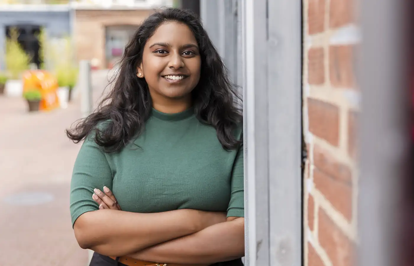 A smiling woman leaning against a brick wall.